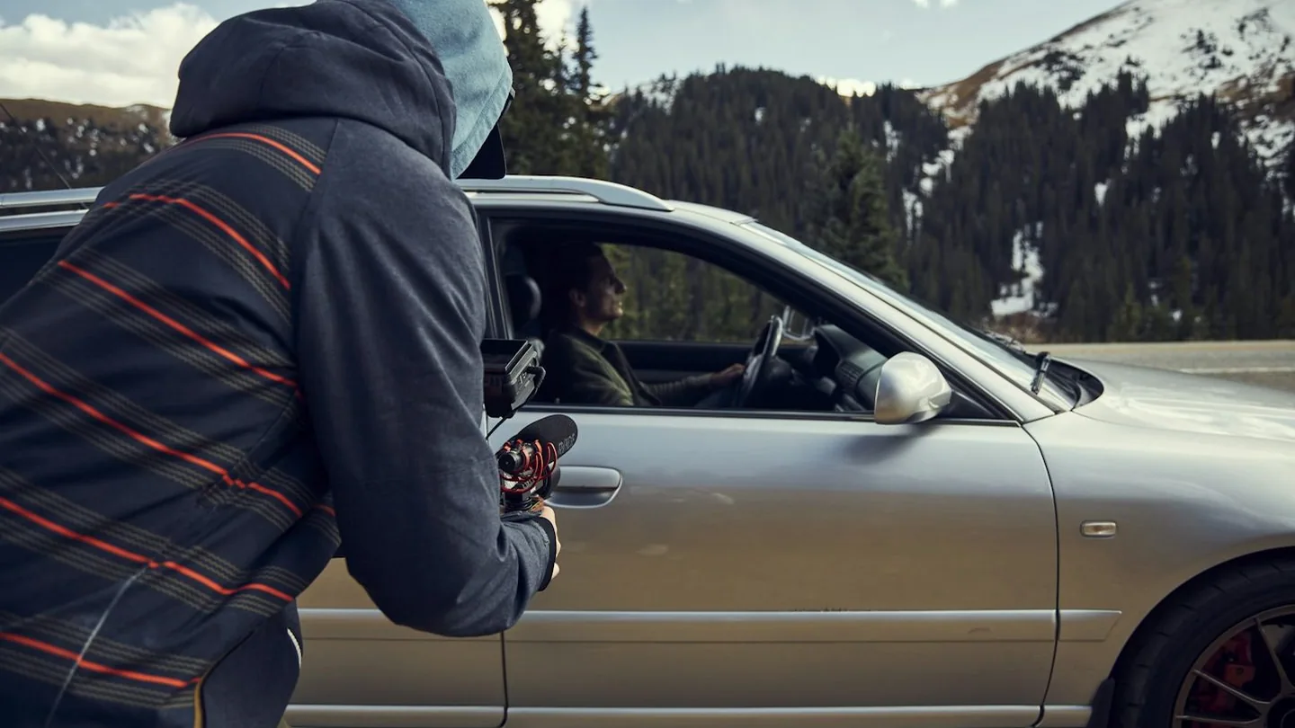 a hooded figure with a device at a car