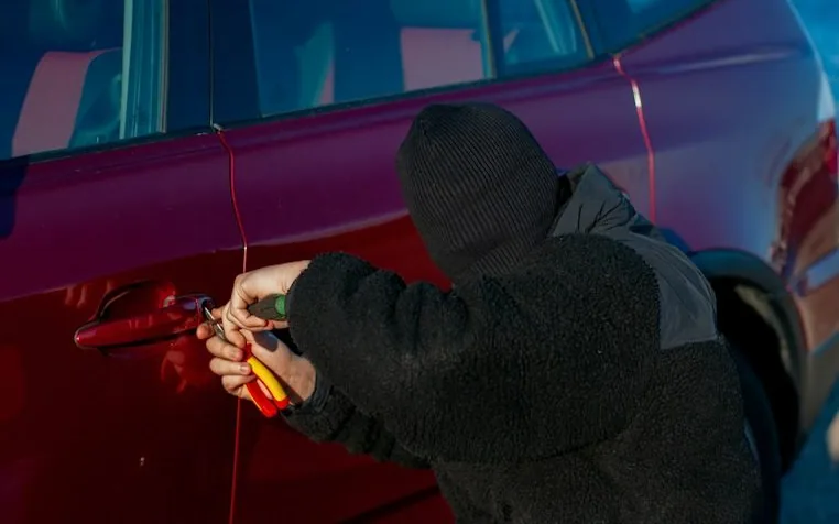 a hooded figure at a car door, face hidden — article card